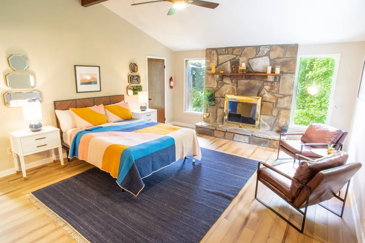 Bedroom with a colorful bedspread, stone fireplace wall, vaulted ceiling and two leather chairs