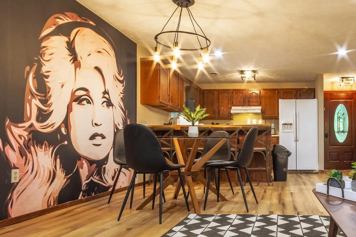 Dining table with four chairs beside a large Dolly Parton mural and the kitchen