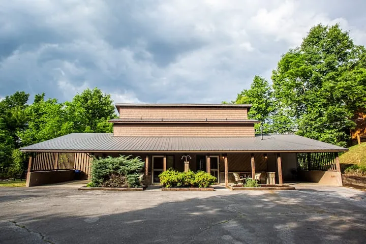 Exterior of the home with a long covered porch, trees and a paved parking area